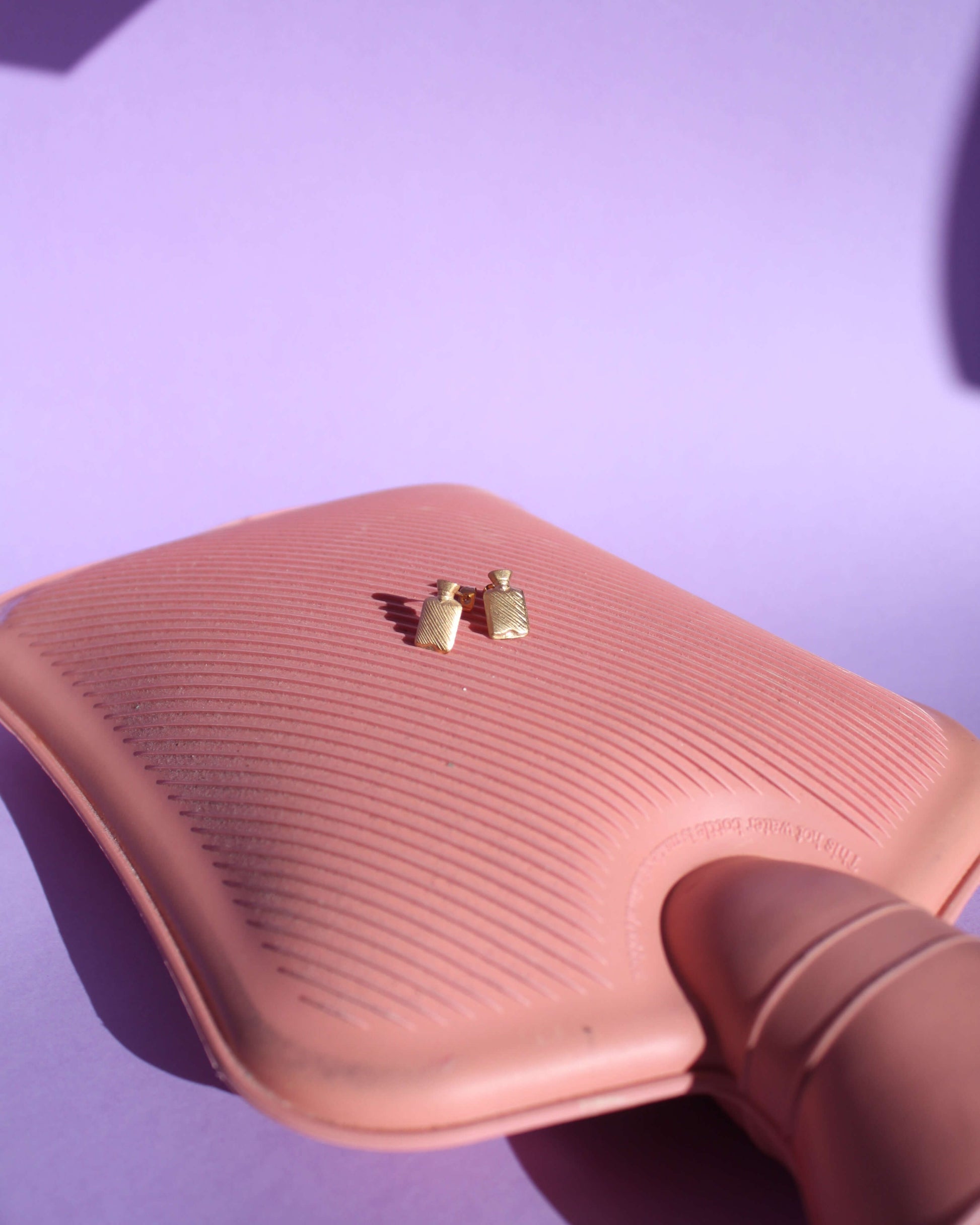 boucles d'oreilles en laiton doré représentant des bouillottes, posées sur une véritable bouillotte