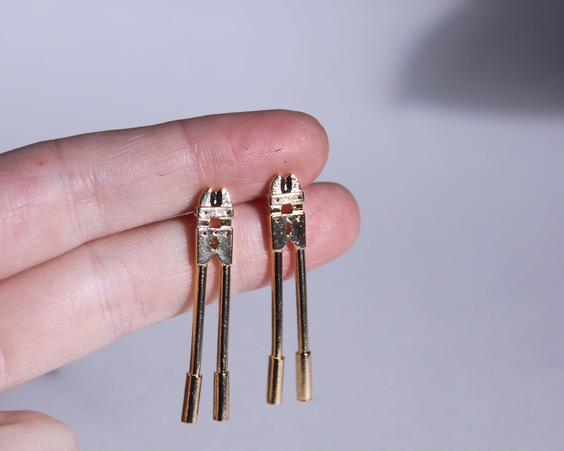 zoom sur une paire de boucles d'oreilles en laiton plaqué or représentant des coupe boulons