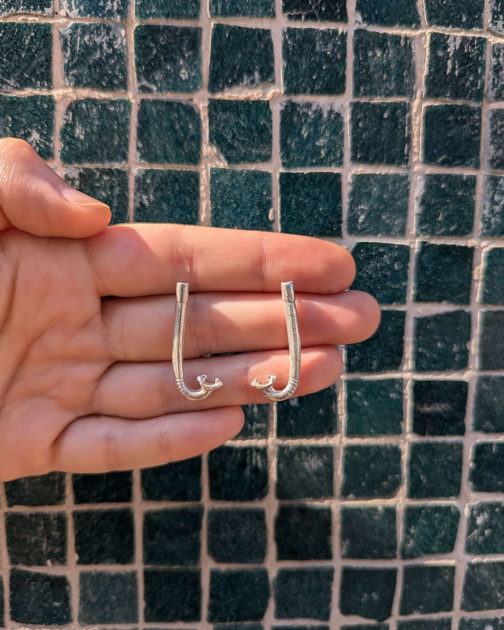 boucles d'oreilles en argent massif en forme de tuba sur un fond à carreaux