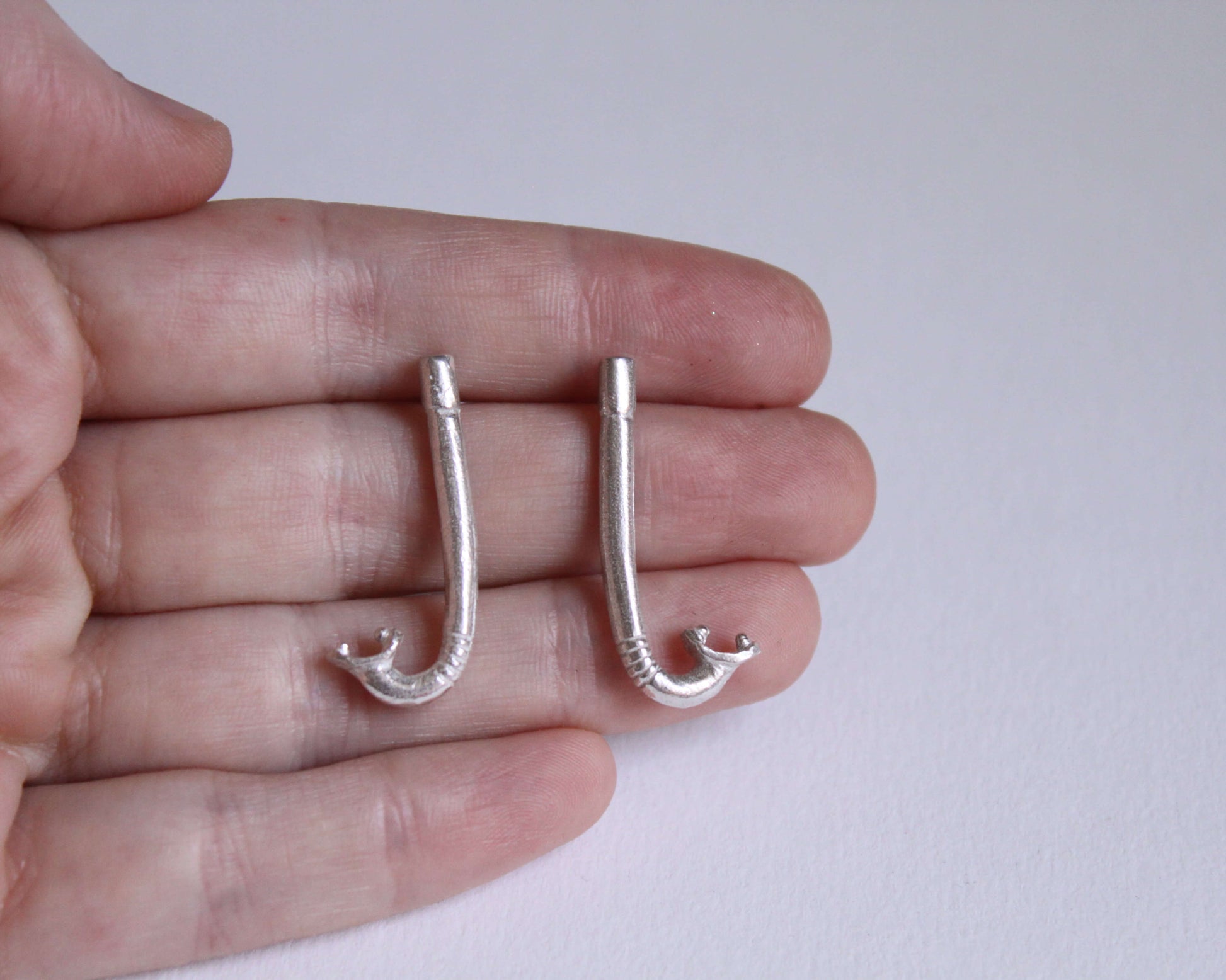 paire de boucles d'oreilles en argent massif en forme de tuba, dans une main