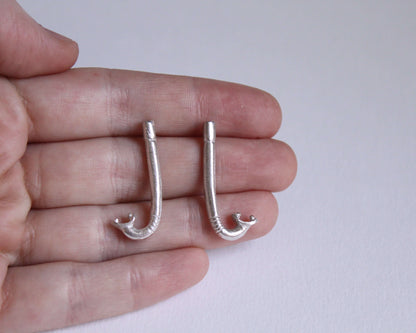 paire de boucles d'oreilles en argent massif en forme de tuba, dans une main