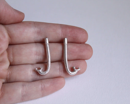 paire de boucles d'oreilles en argent massif en forme de tuba, dans une main